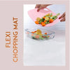Pink flexible cutting mat transferring chopped vegetables into a glass dish; a non-slip, dishwasher-safe kitchen tool.