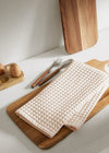 Waffle Pack of 3 kitchen towels in soft beige, neatly folded on a wooden cutting board with cutlery and eggs.