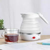 Portable white Folding Electric Kettle next to a glass cup of tea on a desk for travel and office use.