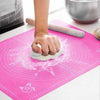 Pink silicone baking mat with measurement guides for kneading dough and rolling pastry on a kitchen countertop.