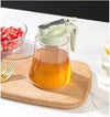 Glass honey bottle with a green lid and handle on a wooden cutting board, perfect for kitchen syrup storage.