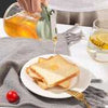 Glass honey bottle drizzling fresh golden honey onto a slice of toasted bread for breakfast.