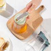 Glass honey bottle with a press-top dispenser lid on a wooden serving board for easy kitchen storage.