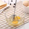 Manual egg beater mixing raw eggs in a glass bowl on a kitchen counter for baking and cooking.