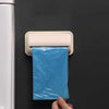 Wall-mounted garbage bag storage box and adhesive kitchen bag dispenser dispensing a blue plastic bag.