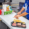 Disposable Cutting Board Mats with sliding cutter used for preparing charcuterie at an outdoor tailgate party.