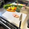 Disposable Cutting Board Mats with sliding cutter used to chop raw chicken and fresh vegetables on a kitchen counter.