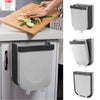 Foldable hanging trash can mounted on kitchen cabinet door for easy food waste disposal while chopping vegetables.