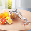 Strong metal hand juicer, small manual citrus press for extracting fresh orange and lemon juice on a wooden table.