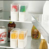 Stackable fridge organizer bin with lid, clear food storage container filled with snacks and cheese slices on shelf.